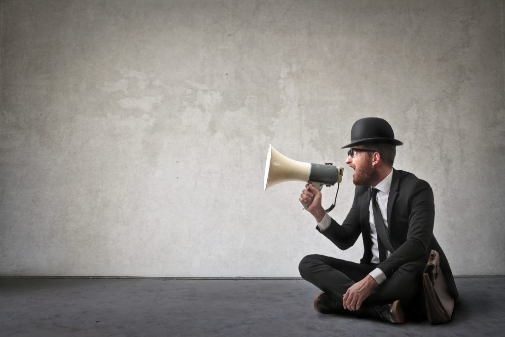 businessman in hat yelling into megaphone