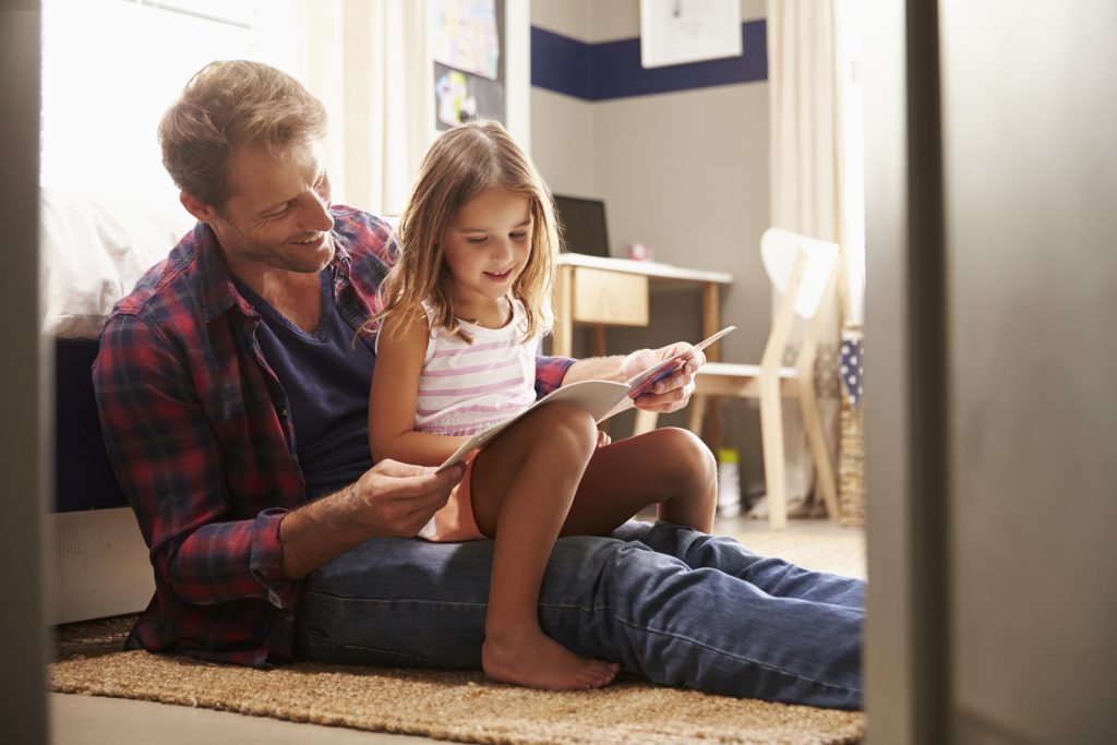Father and young daughter reading together in bedroom