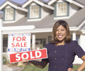 real estate agent holding sold sign next to home