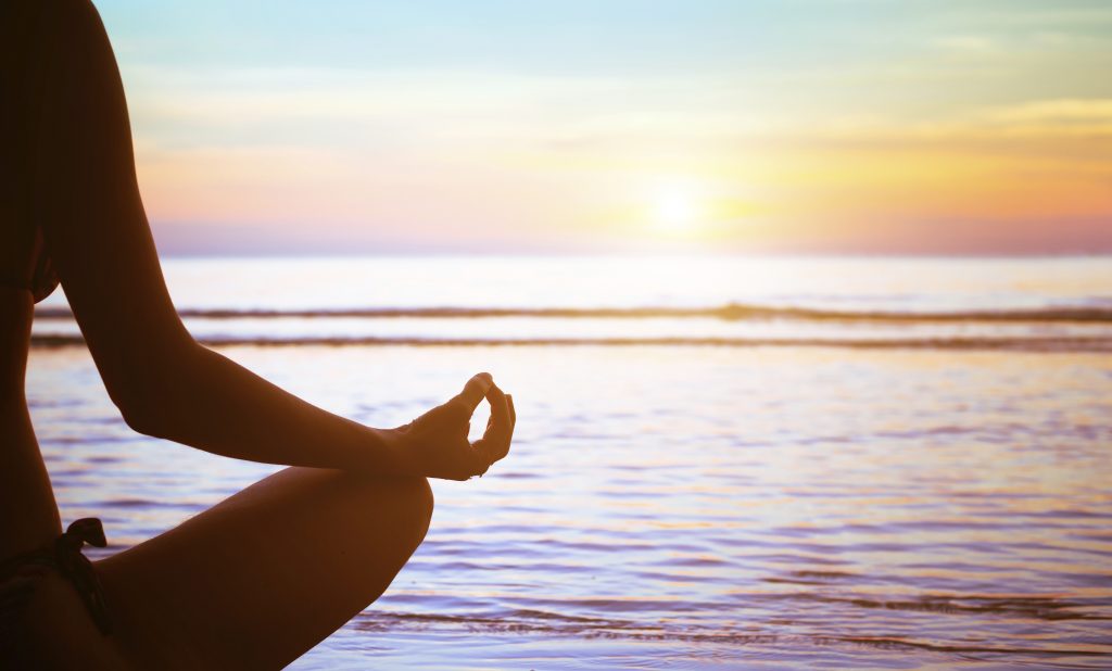 Woman meditating in from of the ocean