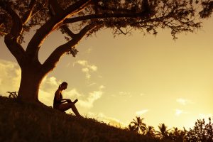 Woman on grass hill working under a tree