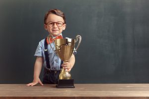 Little boy with glasses holding a golden trophy