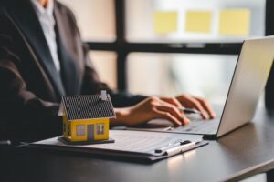 Model of house sitting on side of laptop while real estate professional sends prospecting emails to seller leads