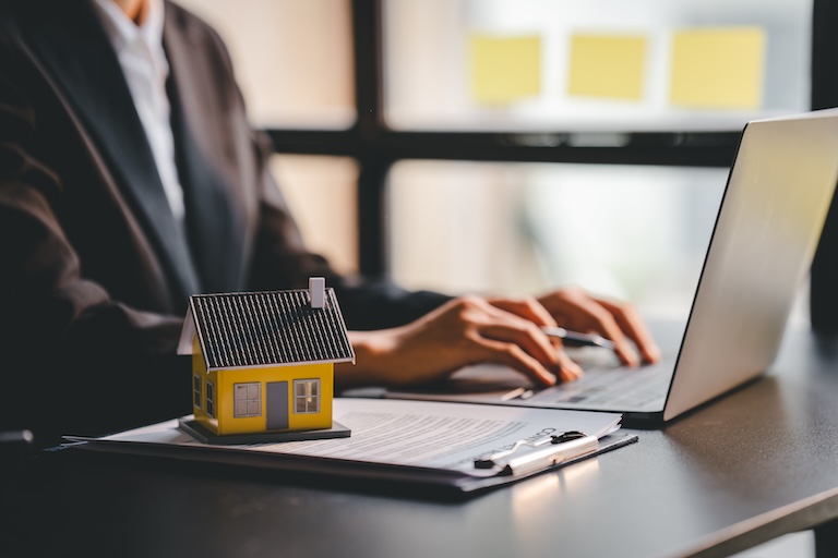 Model of house sitting on side of laptop while real estate professional sends prospecting emails to seller leads