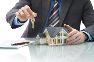 ThinkstockPhotos-475902363 Real estate agent holding key next to figurine of house