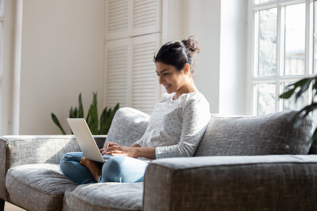 Young woman on couch looking at computer smiling