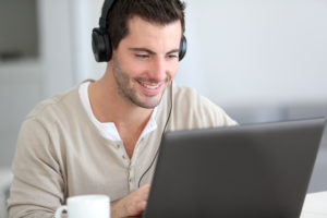 young man on computer smiling with headphones on