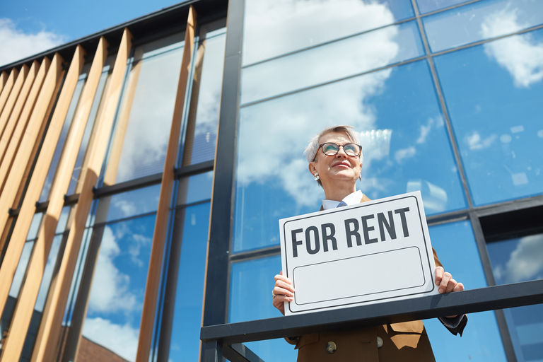 Woman holding a "for rent" sign in front of a commercial building