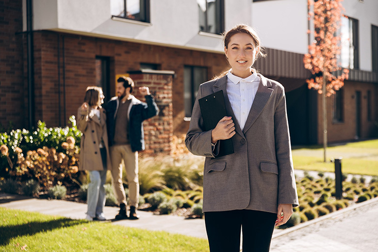 Female real estate agent stands in front of homeowners celebrating the sale of their home