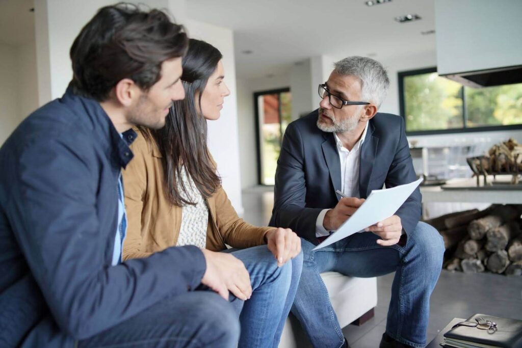 a real estate agent explaining something to a couple sitting on a sofa inside a house