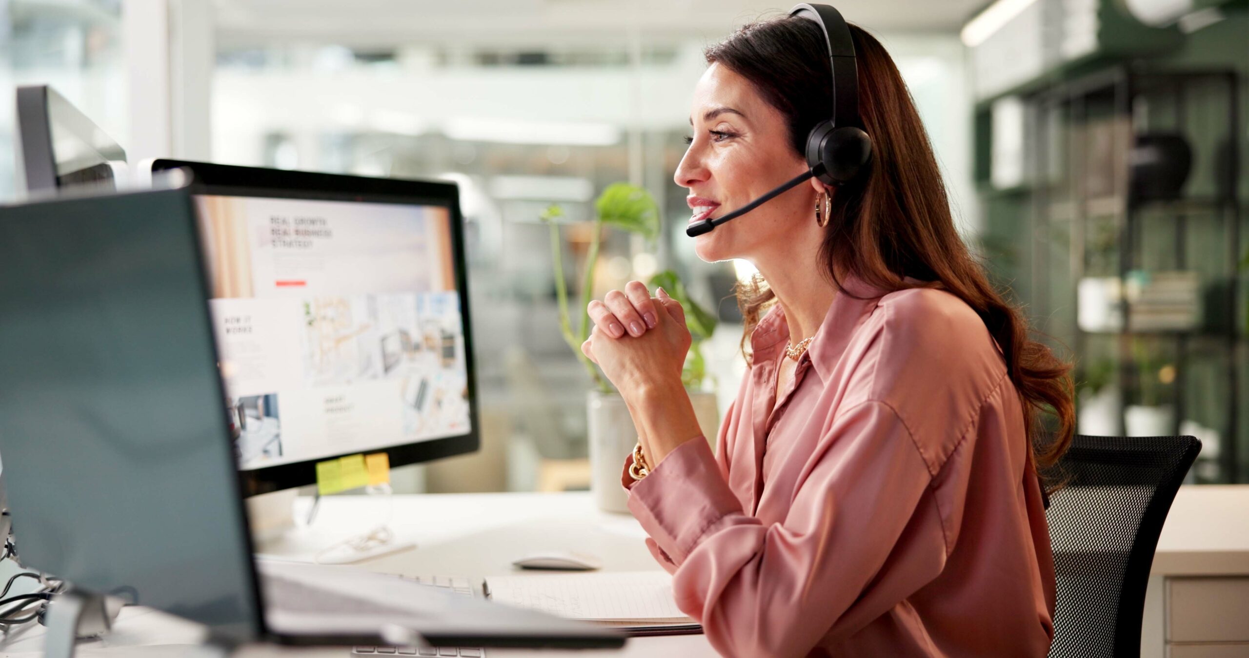 female real estate agent sitting at a desk in front of a computer, talking to a customer using a headset