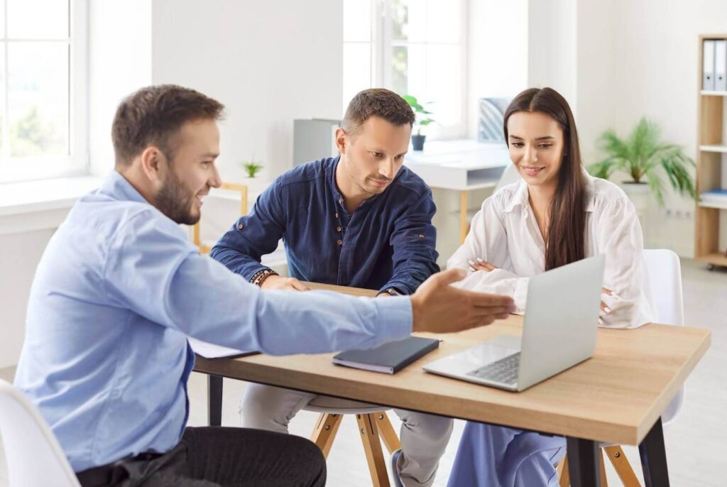 real estate agent during a listing presentation with a young couple sitting around a table, pointing at an open laptop