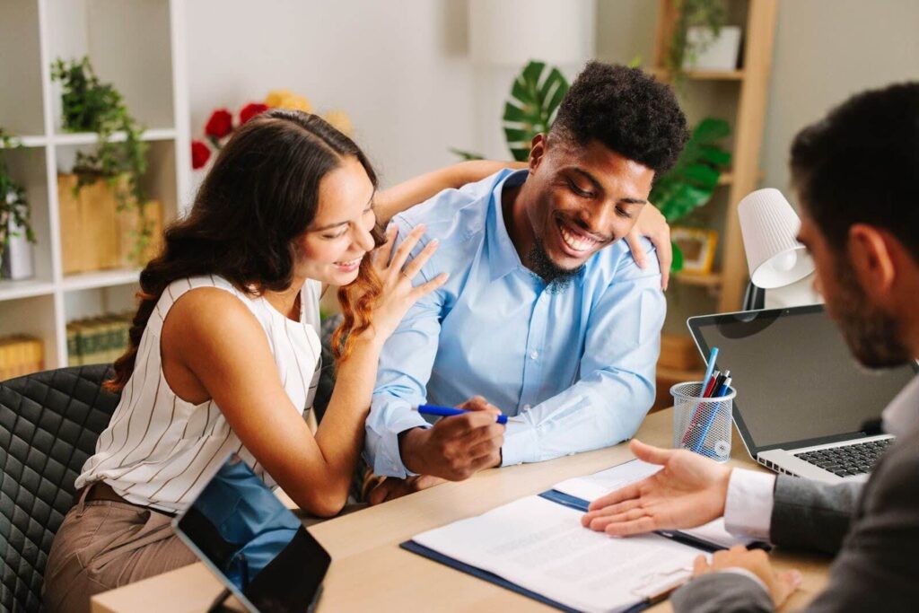 young couple ready to sign an offer presented by a real estate agent sitting across them in an office